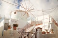 Fira town street with white houses and blue shutters. Cozy hotel building with a white windmill