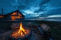 Fire burning in fire pit with wooden chairs and modern log cabin overlooking the ocean at sunset