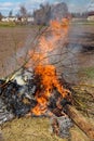 A fire burns brightly against a rural backdrop. Illegal burning of leaves and dry grass Royalty Free Stock Photo