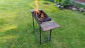 The fire burns in a metal brazier standing on a grassy lawn. The wood is burning to coals that will be used for cooking. At the ed Royalty Free Stock Photo