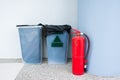 Fire extinguisher on floor beside plastic rubbish bin at building corner background Royalty Free Stock Photo