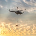 A fire fighter helicopter with a full basket of water flies against a beautiful sunset sky Royalty Free Stock Photo