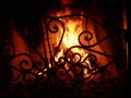 Fire in the fireplace behind a beautiful wrought iron grate with curls. A fire is burning in the fireplace. Night and Royalty Free Stock Photo