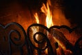 A fire in the fireplace behind a beautiful wrought iron grill with curls. Romantic night with fire in the dark Royalty Free Stock Photo