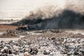 Fire at garbage dump, black smoke from burning old tyres and bulldozer fighting fire Royalty Free Stock Photo