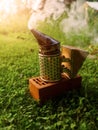 Fire in metal bee smoker standing on a brick and green grass . Agriculture equipment. Selective focus