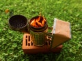 Fire in metal bee smoker standing on a brick and green grass . Agriculture equipment. Selective focus