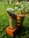 Fire in metal bee smoker standing on a brick and green grass . Agriculture equipment. Selective focus