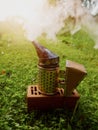 Fire in metal bee smoker standing on a brick and green grass . Agriculture equipment. Selective focus