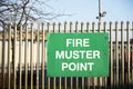 Fire muster assembly point sign at workplace car park fence