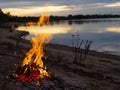 Fire on a sandy beach, large flames on the background of a lake and forest. night sky. outdoor recreation concept