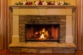 Fire in a stone fireplace decorated with red and white flowers.