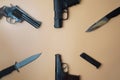 Firearms laid out along a circle. Three guns pistols, cartridges, army knives close-up on a neutral beige background. copy space