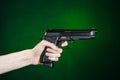 Firearms and murderer topic: human hand holding a gun on a dark green background in studio