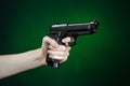 Firearms and murderer topic: human hand holding a gun on a dark green background in studio