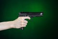 Firearms and murderer topic: human hand holding a gun on a dark green background in studio