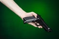 Firearms and murderer topic: human hand holding a gun on a dark green background in studio