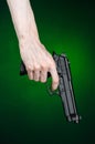 Firearms and murderer topic: human hand holding a gun on a dark green background in studio