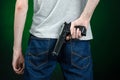 Firearms and murderer topic: man in a gray t-shirt holding a gun on a dark green background in studio