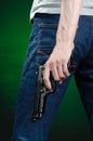 Firearms and murderer topic: man in a gray t-shirt holding a gun on a dark green background in studio
