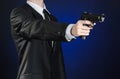 Firearms and security topic: a man in a black suit holding a gun on a dark blue background in studio Royalty Free Stock Photo