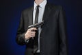 Firearms and security topic: a man in a black suit holding a gun on a dark blue background in studio