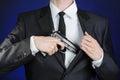 Firearms and security topic: a man in a black suit holding a gun on a dark blue background in studio isolated