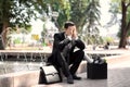 Fired office worker with personal stuff sitting near fountain outdoors