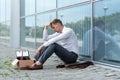 A fired office worker sits on the floor near a modern office building.