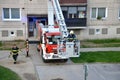 Firefighter begin to uprise into telescopic boom basket of fire truck, block of flats in background