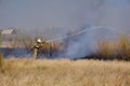 Firefighter extinguishes burning, dry grass from fire hose