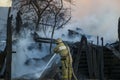 Firefighter extinguishes the fire. Fireman holding hose with water, watering strong stream of burning wooden structure in smoke. Royalty Free Stock Photo