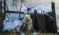 Firefighter extinguishes the fire. Fireman holding hose with water, watering strong stream of burning wooden structure in smoke. Royalty Free Stock Photo