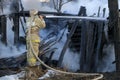 Firefighter extinguishes the fire. Fireman holding hose with water, watering strong stream of burning wooden structure in smoke. Royalty Free Stock Photo