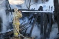 Firefighter extinguishes the fire. Fireman holding hose with water, watering strong stream of burning wooden structure in smoke. Royalty Free Stock Photo