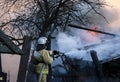 Firefighter extinguishes the fire. Fireman holding hose with water, watering strong stream of burning wooden structure in smoke. Royalty Free Stock Photo