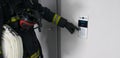 A firefighter in protective clothing, with fire extinguishing equipment, tries to open a closed door by dialing the intercom code Royalty Free Stock Photo