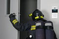 A firefighter in protective clothing and a hard hat, with fire extinguishing equipment, enters the doorway, rear view Royalty Free Stock Photo