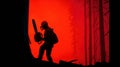 Firefighter Cuts Tree With Chainsaw During Wildfire, Wearing Protective Gear, Silhouetted Against Hazy Red Sky at Dusk Royalty Free Stock Photo