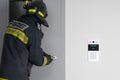 A firefighter is trying to open the iron entrance door in the entrance, next to an intercom with video surveillance Royalty Free Stock Photo