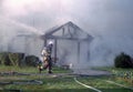 A firefighter walks in front of a building that is onm fire