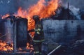 Firefighter walks in front of a small buildig on fire