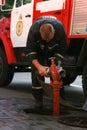 Firefighters connect hoses to a hydrant on the street near a burning building. Extinguishing a burning building