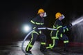 Firefighters using a water hose to eliminate a fire hazard. Team of female and male firemen in dangerous rescue mission