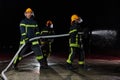 Firefighters using a water hose to eliminate a fire hazard. Team of female and male firemen in dangerous rescue mission