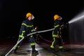 Firefighters using a water hose to eliminate a fire hazard. Team of female and male firemen in dangerous rescue mission