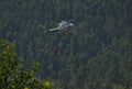 Firefighting and rescue helicopter with bucket of Bambi carrying water to put out a forest fire with mountain background. Copy