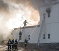 Fireman fighting a fire with a hose at the top of a ladder.