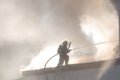 Fireman fighting a fire with a hose at the top of a ladder