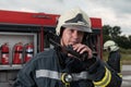fireman using walkie talkie at rescue action fire truck and fireman& x27;s team in background.